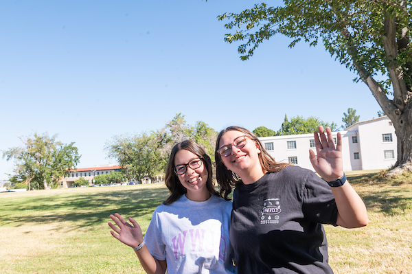 two female students waving to the camera while standing in the grass on move-in day